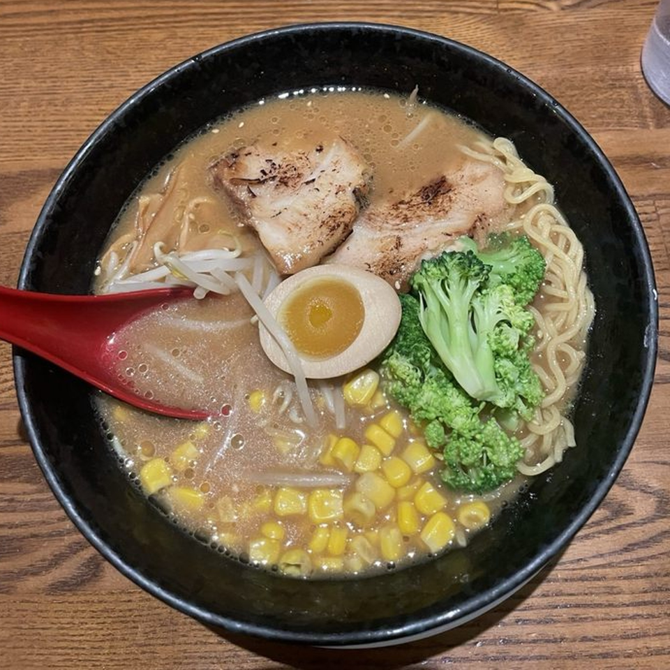 A black bowl of Huntington Ramen & Sushi ramen with pork, egg, broccoli, corn, and bean sprouts.