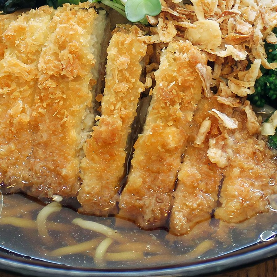 Close-up of sliced, breaded fried pork cutlet (tonkatsu) in a ramen bowl with broth and noodles.